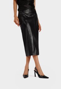 Gonna midi in pelle nera con una texture liscia e una sottile lucentezza. Abbinata a tacchi a punta nera in vernice con design slingback.