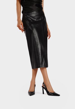 Gonna midi in pelle nera con una texture liscia e una sottile lucentezza. Abbinata a tacchi a punta nera in vernice con design slingback.