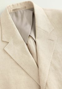 Blazer en lin beige avec un col cranté, doublure beige lisse et détails de couture fines sur les revers et les poches.
