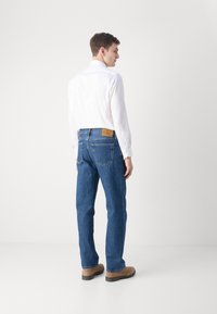 Chemise blanche légère associée à un jean en denim bleu. Accents en cuir marron à la taille et bottes marron décontractées.