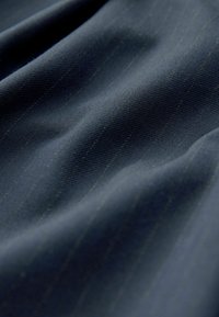 Námořnická látka s jemnými pruhy, disponující hladkou strukturou a mírným leskem, která vykazuje volně splývající záhyby naznačující pružnost.