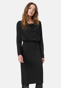 Zwart langslachtig jurk met een colkraag, elastische taille en slanke pasvorm. Soepele, rekbare stof met een lengte tot halverwege de kuit.