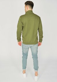 Zielona bluza polarowa z wysokim kołnierzem, ściągaczami przy rękawach i w pasie; zestawiona z jasnoniebieskimi dżinsami i białymi sneakersami.