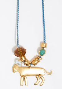 Collana in tonalità oro con pendente a forma di gatto, cordino intrecciato blu e diverse perline decorative in ambra, verde e bianco.