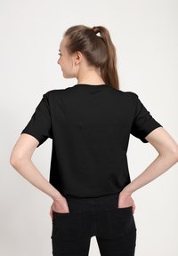 Černé bavlněné tričko s krátkým rukávem a kulatým výstřihem, zobrazené ze zadu. Tkanina vypadá hladce, bez viditelných vzorů nebo akcentů.