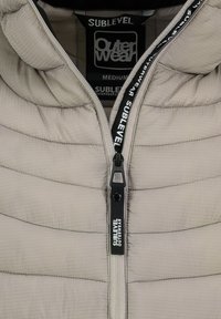 Beige Daunenjacke mit horizontaler Steppoptik, Stehkragen und schwarzem Reißverschluss mit Logodetails. Größentag in Medium sichtbar.