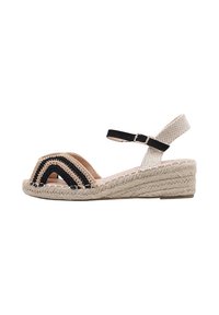Sandalia cuña con punta abierta, superior tejido en beige y negro, correa ajustable al tobillo y suela envuelta en yute. Diseño texturizado en la parte superior.