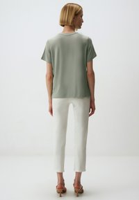 Blusa corta a maniche corte verde chiaro con una vestibilità comoda; abbinata a pantaloni bianchi a gamba dritta e sandali beige, che mostrano un design elegante e minimal.