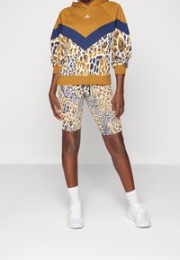 Gul och marinblå hoodie med djurtryck, dragskoärmar, parat med matchande mönstrade cykelbyxor. Vita sneakers och strumpor fulländar outfiten.
