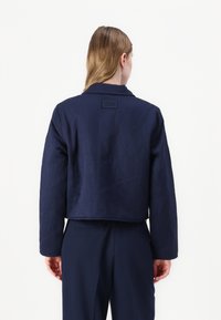 Kort navy jasje van geweven stof met een kraag en labeldetails aan de achterkant. Heeft lange mouwen en een rechte zoom.
