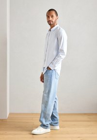 Gestreiftes Hemd in Hellblau, lässige hellblaue Jeans und weiße Sneakers, vor einem neutralen Hintergrund präsentiert.