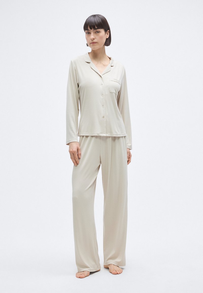 Σετ μπεζ πυτζάμες με πουκάμισο μακρυμάνικο με κουμπιά και τσέπη, καθώς και φαρδιά παντελόνια. Κατασκευασμένο από λεία, ελαφριά ύφασμα.