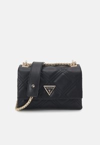 Zwarte, gequilt leren Guess-handtas met gouden kettingband en driehoekig metalen logo op de voorflap tegen een witte achtergrond.