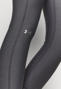 Czarne legginsy sportowe o gładkiej fakturze, z dopasowanym krojem, bocznymi szwami i małym szarym logo Under Armour w pobliżu łydki.