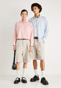 Ribade kraepe roosa ja sinise triibuga, beežid lühikesed püksid kontrastsete sääreosadega, mustad kingad ja must käekott.