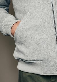Gray zip-up sweatshirt in textured fabric with ribbed cuffs and waistband; features side pockets and a smooth zipper.