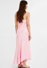 Rosa satängmaxiklänning med spagettistappar, en blommig textur och en asymmetrisk nederkant, med en lätt design och en slät yta.