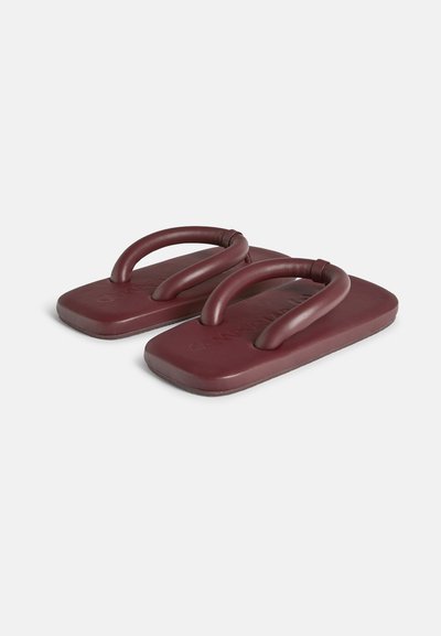 Burgundy flip-flops med dubbla böjda remmar, med en texturerad sula och en rektangulär fotbädd. Tillverkad av flexibel och hållbar material.