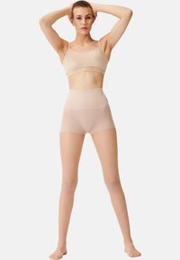 Nudefarbener nahtloser BH und hochgeschnittenes Shorts-Set, das aus weichem Stoff, klaren Linien und einer glatten Textur besteht.