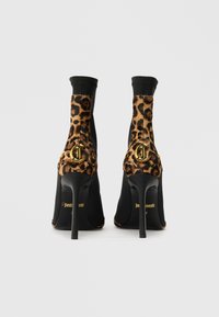 Bottines noires à talons hauts avec des accents en imprimé léopard, présentant un détail de logo doré et un matériau texturé sur le dessus.