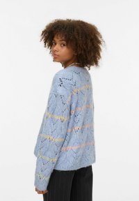 Gaiši zils adīts džemperis ar atvērtu mežģīņu rakstu, kas rotāts ar pasteļrozā un dzeltenām svītrām. Garas piedurknes un brīvs piegriezums.