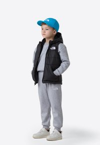 Svart dunvest over grå langermet skjorte og bukser, blå caps, hvite joggesko. Vesten har hette og glidelås foran.