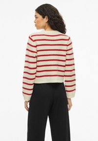 Pull en crochet avec des rayures rouges et blanches, un design court, des poignets côtelés et un col rond, porté avec un pantalon noir.