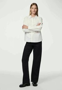 White button-up shirt with a structured collar, long sleeves, and a straight cut. Paired with black wide-leg trousers and black shoes.