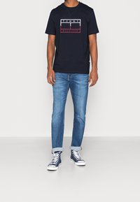 Námořnická modrá bavlněná tričko s logem "TOMMY HILFIGER" v bílé a červené barvě. Spárováno se světle modrými džíny a námořnickými vysokými teniskami.