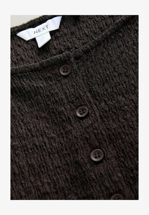 Svart texturerad cardigan med ett krinklat tyg, prydd med fem plastknappar framtill och en etikett som läser "NEXT" vid nacken.