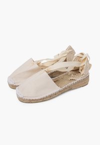 Espadrillas in canvas beige con suola piatta in juta, dotate di punta arrotondata e lacci intrecciati per una chiusura sicura.