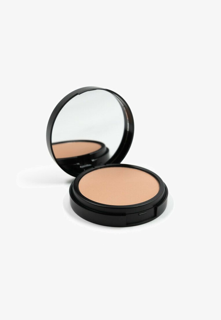 Cipria compatta rotonda con superficie liscia di un beige chiaro, racchiusa in un involucro di plastica nera con uno specchio all'interno.