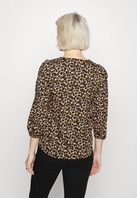 Blusa com padrão de leopardo, mangas três-quartos, decote redondo e um corte ligeiramente relaxado. O tecido possui uma textura suave com coloração em preto e bege.