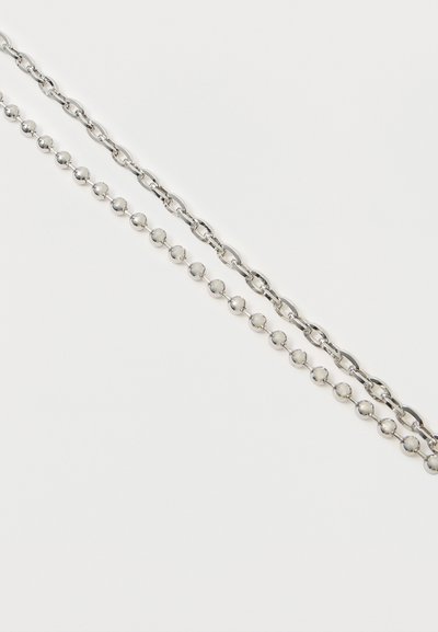 Stříbrné kovové řetězy s různými články: jeden s oválnými články, druhý s kulatými korálky. Hladký povrch a lesklý finiš.