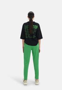 Svart oversized t-shirt med grön text på baksidan, matchad med ljusgröna joggerbyxor. Modellen bär beige sneakers.