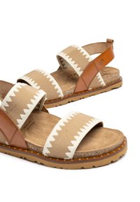 Sandali beige con due ampie cinghie in tessuto caratterizzate da un motivo zigzag bianco, dettagli in pelle marrone e una soletta in sughero testurizzato.