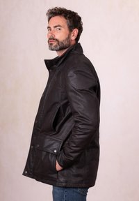 Dark brown leather jacket with a snap collar, side pockets, and padded shoulders, featuring a smooth texture and a tailored fit.