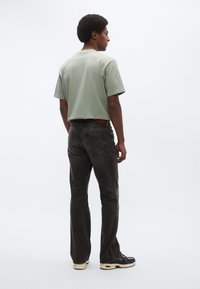 Hellgrünes T-Shirt mit kurzen Ärmeln, kombiniert mit dunkelgrauen Jeans, einem Lederbund-Etikett und schwarzen Sneakers mit mehrfarbigen Akzenten.