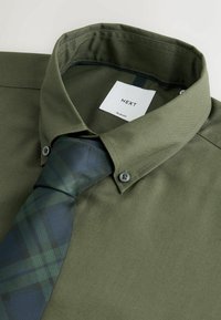 Olijfgroene slim-fit shirt met een spread collar, gecombineerd met een donkergroene geruite stropdas. Bevat twee grijze knopen en een label met de merknaam.