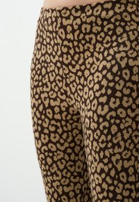 Leggings marroni con motivo leopardato in tonalità beige, realizzati in tessuto morbido con una superficie liscia e una vita elasticizzata per il massimo comfort.
