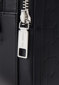 Black handbag featuring a textured design, silver zipper, and a logo tag. Smooth leather material with visible stitching and clean lines.