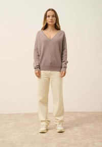 Sweter z dekoltem w serek, z długim rękawem w miękkim, jasnolila materiale, w zestawieniu z luźnymi, kremowymi spodniami i białymi sneakersami. Prosty, luźny krój.