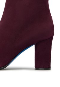 Stivale alla caviglia in suede bordeaux con tacco a blocco, texture liscia e suola blu a contrasto. Il design è elegante e moderno.