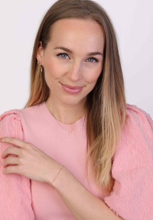 Roze geribbelde top met textuurpofmouwen, gelaagde gouden ketting met een kleine hanger en een delicate gouden armband met kralen.