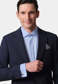 Navy suit jacket with structured lapels and light blue shirt. Features cufflinks on the shirt cuffs and a patterned pocket square in the jacket pocket.