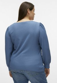 Blå langærmet top med en rund halsudskæring, tekstureret ribbet stof og pufærmer. Bæres med lyseblå jeans.