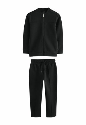 Sort sweatshirt med lynlås og lange ærmer kombineret med sorte joggers med snøre og sømdetaljer, vist på en hvid baggrund.
