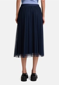 Gonna a balze in tulle blu navy con vita solida, che scende sotto il ginocchio, abbinata a scarpe nere chunky, che mette in mostra una texture stratificata.