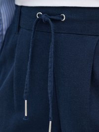 Primo piano di pantaloni blu navy con cordoncino in tessuto annodato in vita, caratterizzato da terminali in metallo.