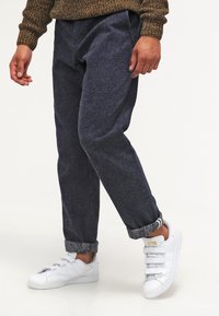Navy blue textured pants with a straight leg design, cuffed at the ankle, paired with white sneakers featuring three Velcro straps.